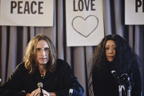 John Lennon, played by Christopher Eccleston, and Yoko Ono, played by Naoko Mori, face the press with peace signs in the background