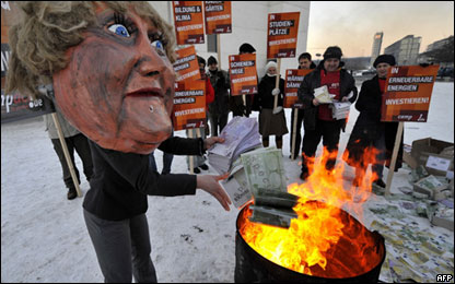 An activist dressed up as German Chancellor Angela Merkel throws fake Euro currency notes in a fire during a protest in front of the chancellery building in Berlin January 12, 2009.