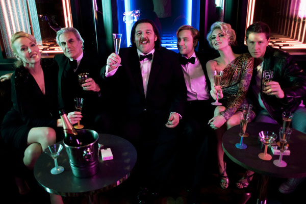 The cast of Money, in character, raise glasses of champagne