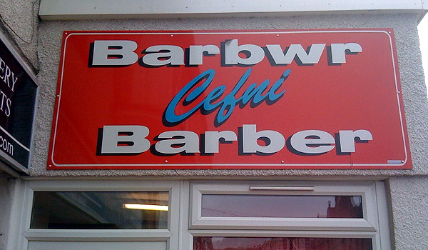 A sign for a barber's shop written in English and Welsh