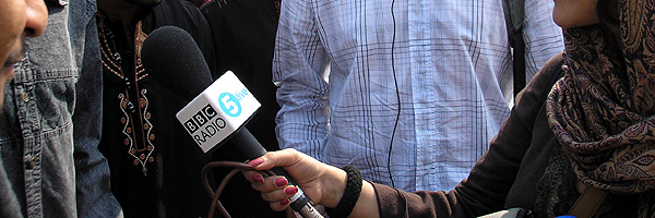 A reporter holding a 5 live microphone out to a crowd during an interview