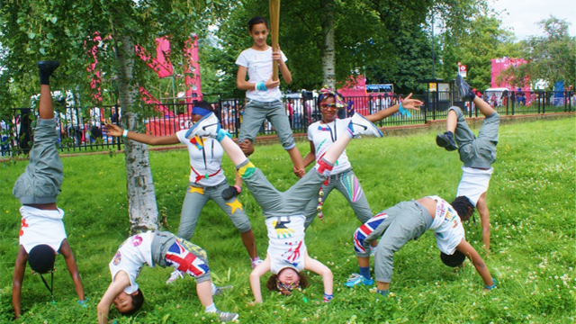 Eight youg adults doing various gymnastics in a playground, forming a pyramid