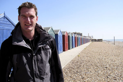 Dan Snow stands in front of multicoloured beach huts on Hastings seafront
