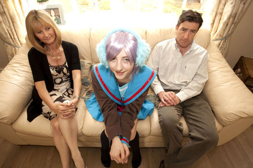 Beckii Cruel, complete with shiny purple wig, sits on the coach with her parents