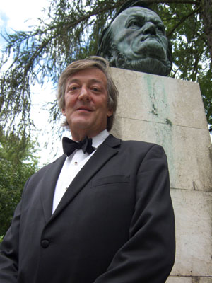 Stephen Fry in a tuxedo stands by a bust of Richard Wagner