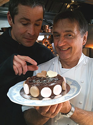 Cameraman Andy Smith stands next to Raymond Blanc, who is holding a chocolate macaroon cake