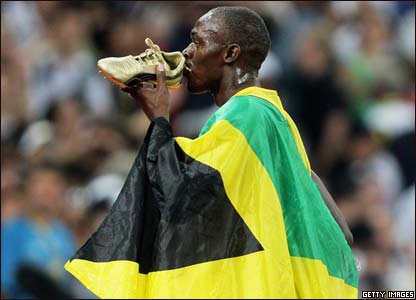 Usain Bolt kisses his trainers while draped in the Jamaican flag